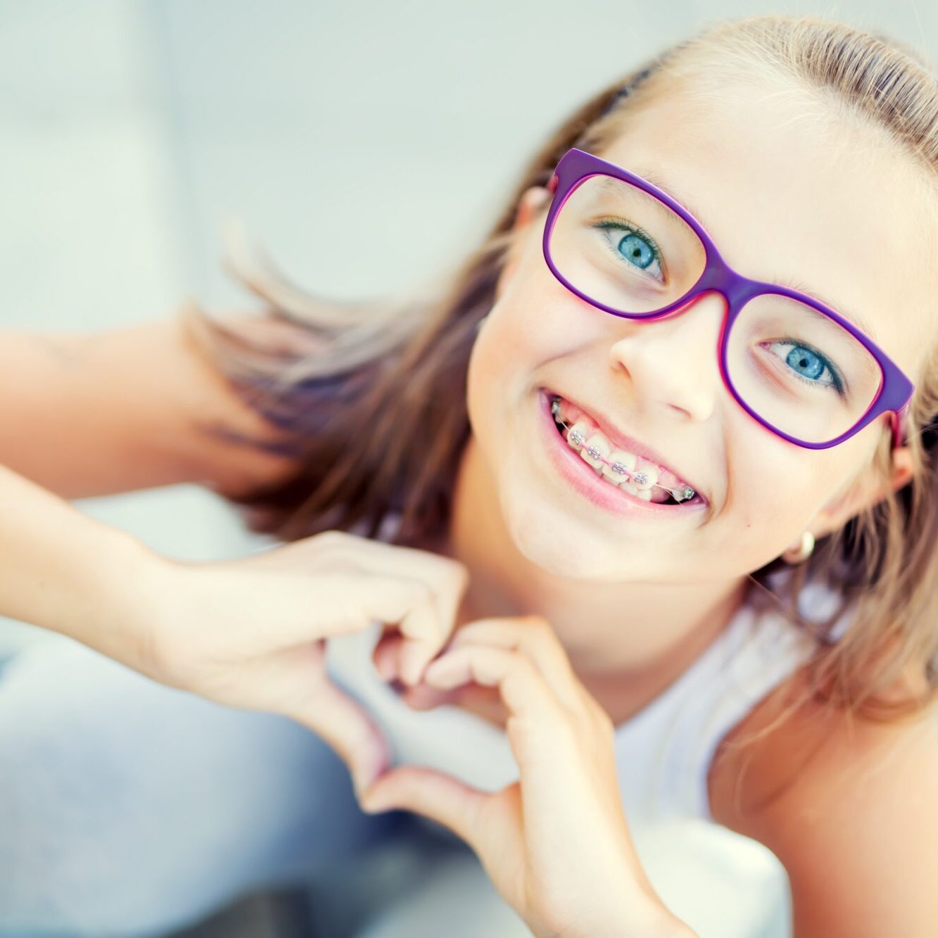 Smiling,Little,Girl,With,Braces,And,Glasses,Showing,Heart,With